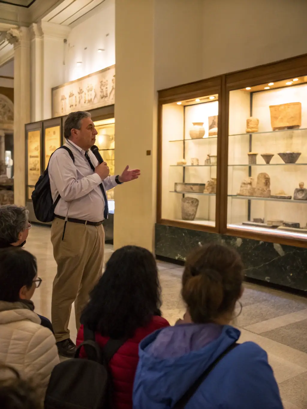 A photograph of a public lecture or workshop on archaeology, with an archaeologist presenting findings to an engaged audience in a community hall.